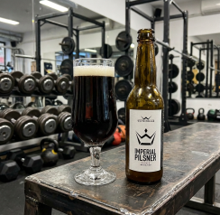 Pahar si sticla de bere neagra pe o banca de fitness ilustrand culoarea inchisa a urinei in caz de rabdomioliza